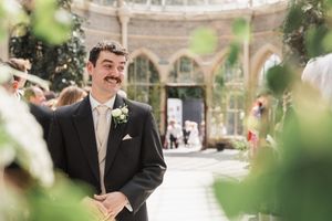 A wedding scene showing someone waiting in anticipation at an outdoor venue with stone archways and greenery.
