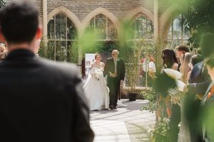 Outdoor wedding ceremony through leaves under natural light and greenery.