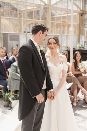 Elegant wedding ceremony taking place in a bright conservatory with glass ceiling and white decor.