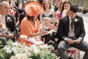 Guest wearing a vibrant orange outfit interacts with a small child during an outdoor wedding ceremony.
