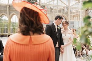 Wedding ceremony in a bright conservatory with coral-colored bridesmaids dresses and floral decor.