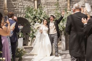 Newlyweds celebrate joyfully under a stone archway adorned with white floral arrangements.