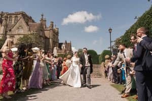 Wedding party exits historic stone building as guests line pathway throwing celebratory confetti.