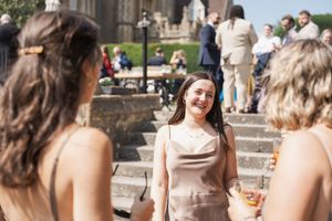 Wedding guests gathered on stone steps outside a historic building on a sunny day.