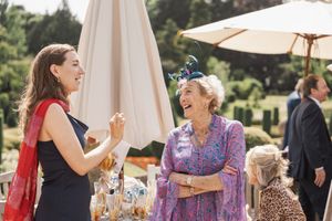 Wedding guests mingle and laugh during an outdoor reception under white umbrellas.