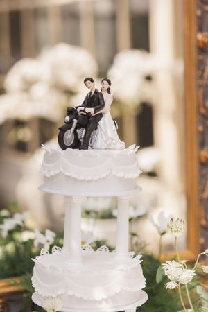 Traditional white tiered wedding cake with figurine toppers displayed at an elegant reception.