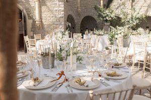 Elegant white table settings and floral centerpieces arranged for a wedding reception in a bright stone venue.