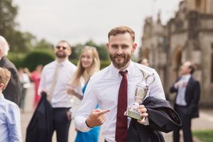 Guest in burgundy tie enjoys drinks during outdoor wedding reception.