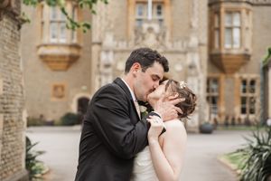 A romantic moment captured between newlyweds against a historic stone building backdrop.