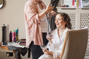 Professional hairstylist works on client's hair in a salon while client enjoys coffee.