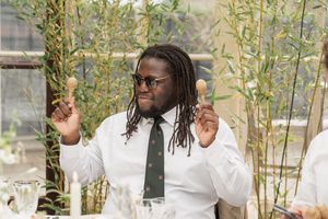 Wedding guest in white shirt and tie gestures enthusiastically during outdoor celebration.
