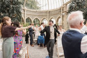 Wedding guests celebrate on the dance floor of an indoor conservatory venue.