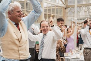 Wedding guests celebrate with enthusiastic dancing and raised arms during reception.