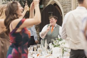 Wedding celebration outdoors with guests raising glasses in a toast near a stone archway.