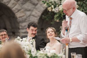 Wedding guests sitting at an elegant outdoor reception with floral centerpieces and white table settings.
