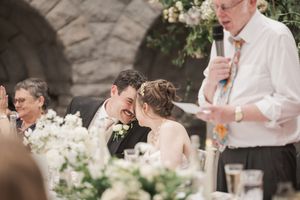 An intimate moment during a wedding reception with elegant white floral centerpieces and stone architecture.