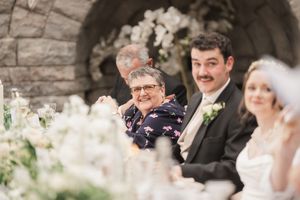 Wedding reception scene with elegant table settings and white floral arrangements under stone arches.