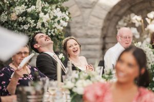 Joyful laughter shared during wedding reception under stone archway with floral decorations.