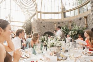 Wedding reception dinner setup in an elegant greenhouse with table settings and floral decor.