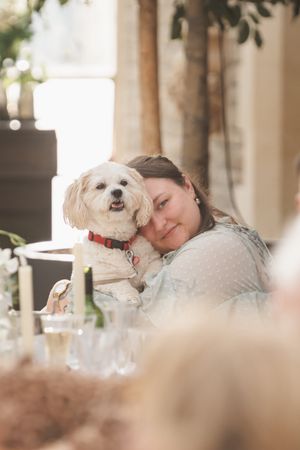 A white fluffy dog cuddling with someone during a wedding reception.