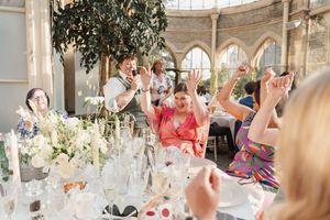 Wedding reception celebration in a light-filled conservatory with decorated tables and excited guests.