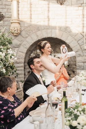 Reception guests laughing and fanning themselves while seated at outdoor tables.