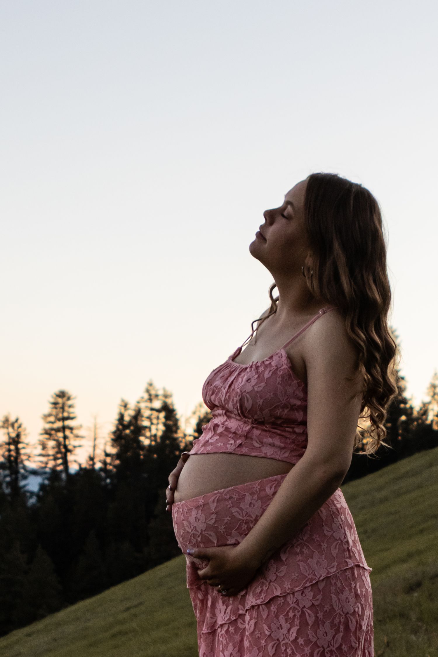 Mountainside maternity session in Talent, Oregon. Subject is wearing a pink two piece, has light skin and long brown hair.