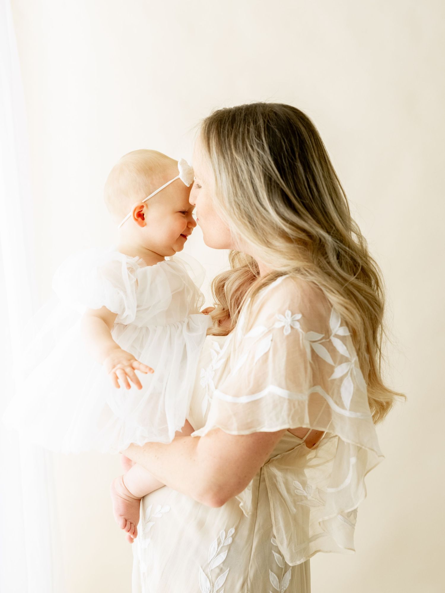 A tender moment captured in soft light as parent and baby in matching white outfits share an intimate bonding moment.