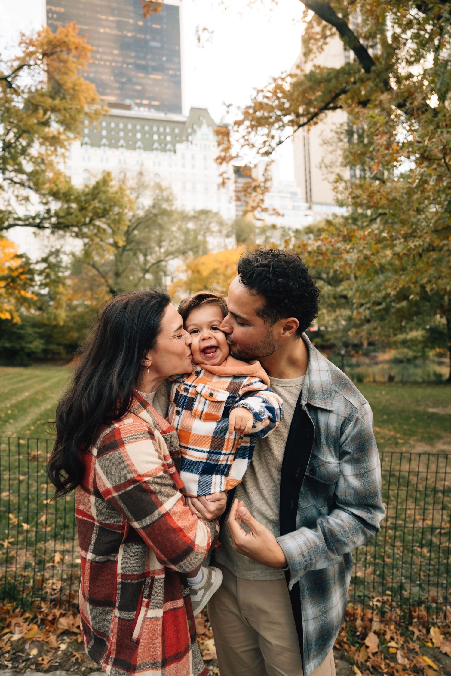 A family walks together on a tree-lined park path with outstretched arms on an autumn afternoon.