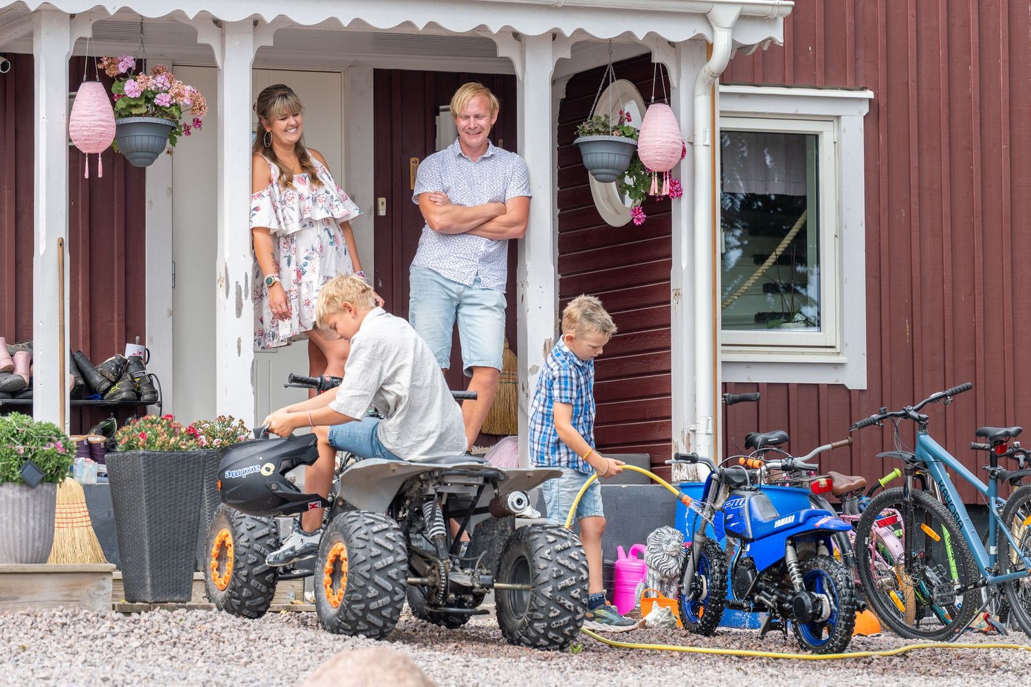 Familjebild av det annorlunda slaget. Två vuxna som står på farstun och tittar glatt på sina barn som tvättar och pysslar med sina fordon.