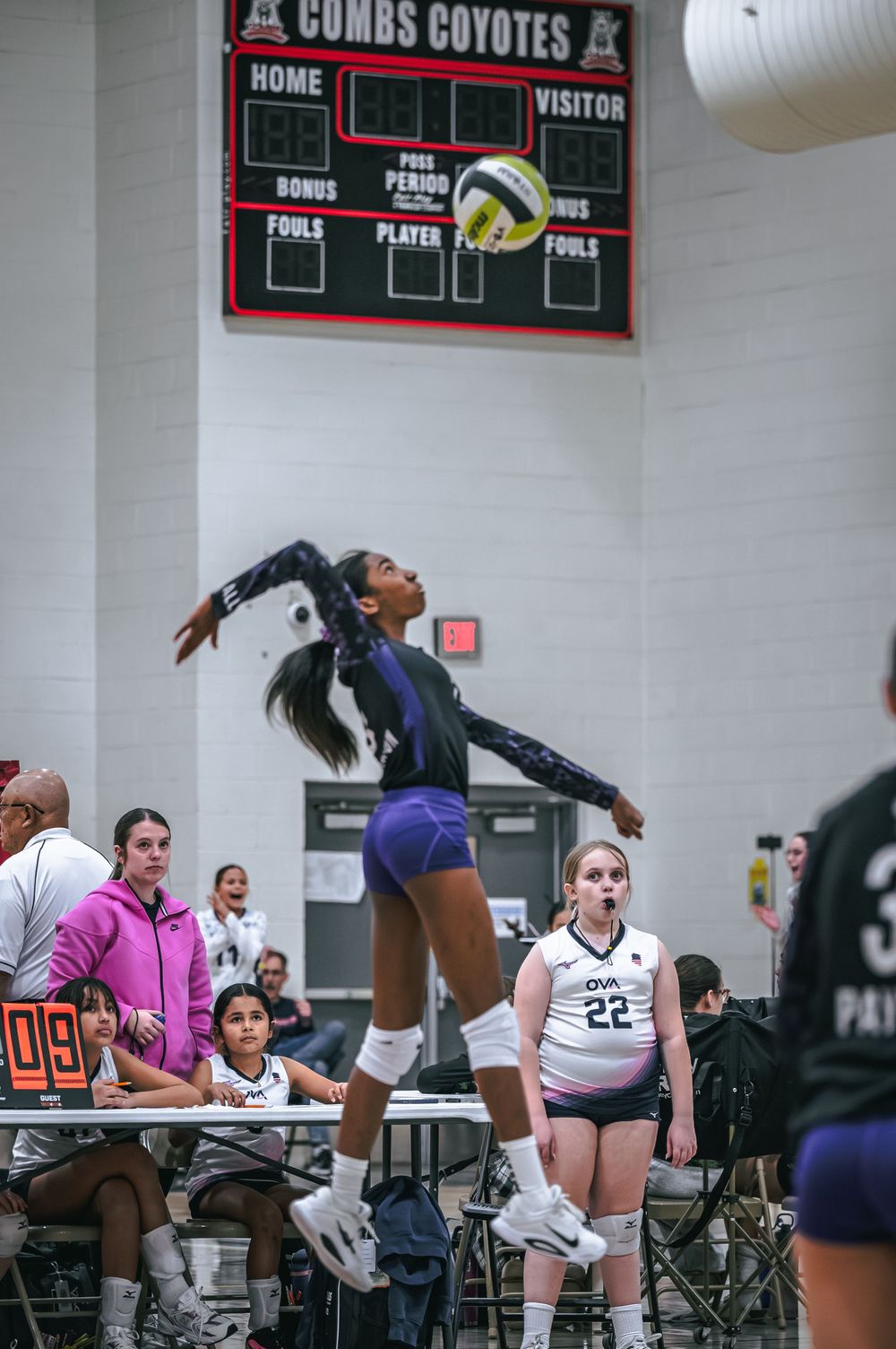 Volleyball player leaps to serve the ball at Combs Coyotes gymnasium during a match.