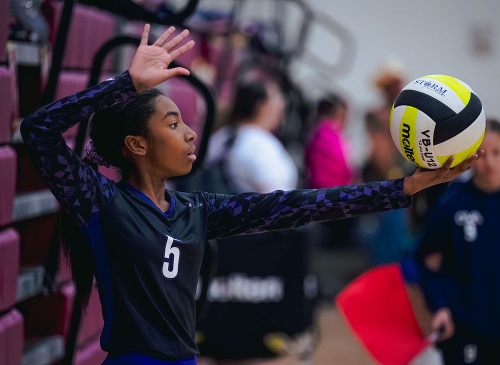A female volleyball player wearing number 5 prepares to serve the ball during a match.