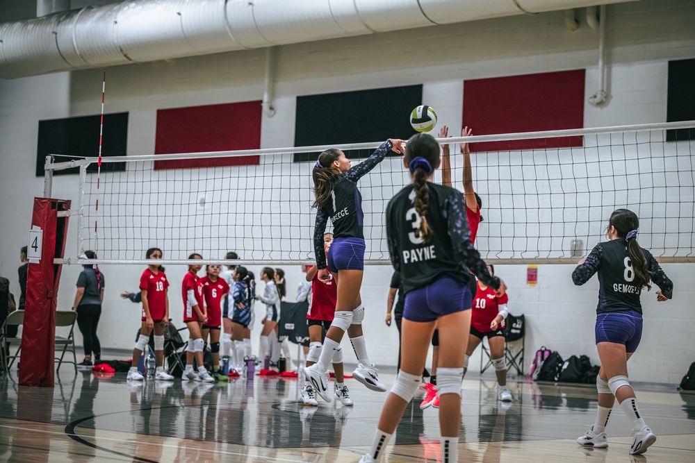 Volleyball players compete at the net during an indoor youth volleyball tournament game.