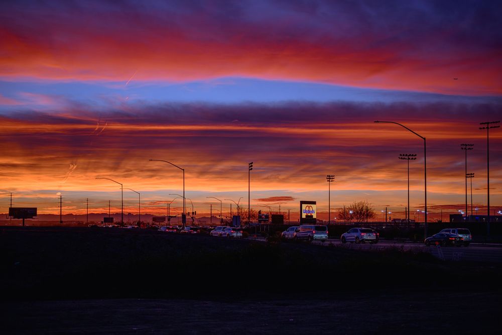Dramatic vibrant red and purple sunset sky over a silhouetted urban highway and buildings.