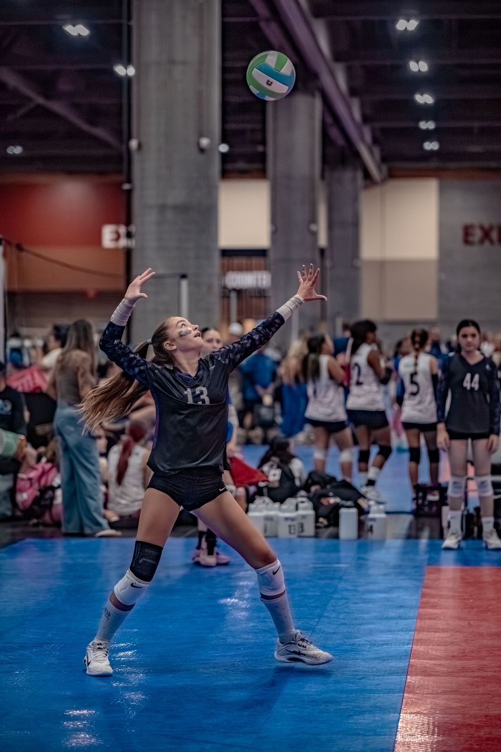 Player #13 serves a volleyball during an indoor tournament match.