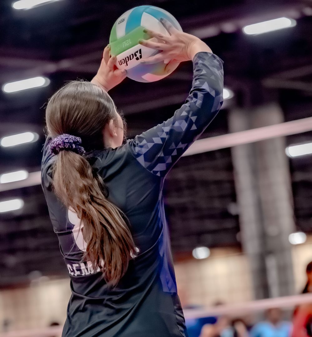 Female volleyball player sets the ball overhead with both hands during an indoor volleyball tournament game.
