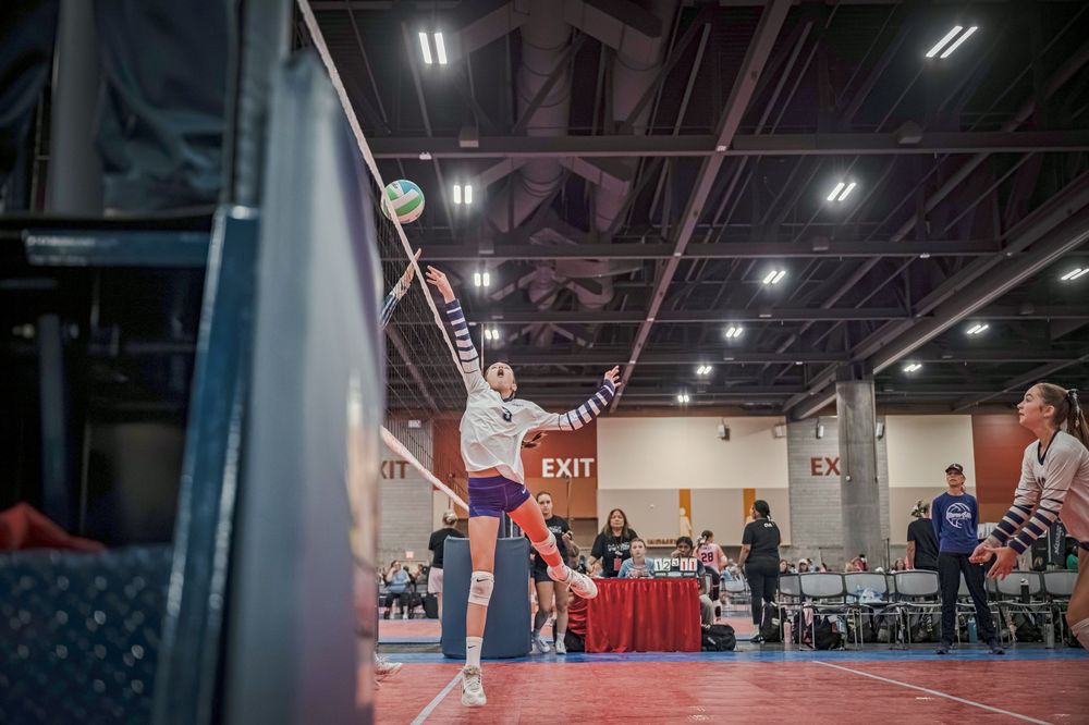 Female volleyball player jumping to spike the ball during an indoor tournament match in a sports facility.