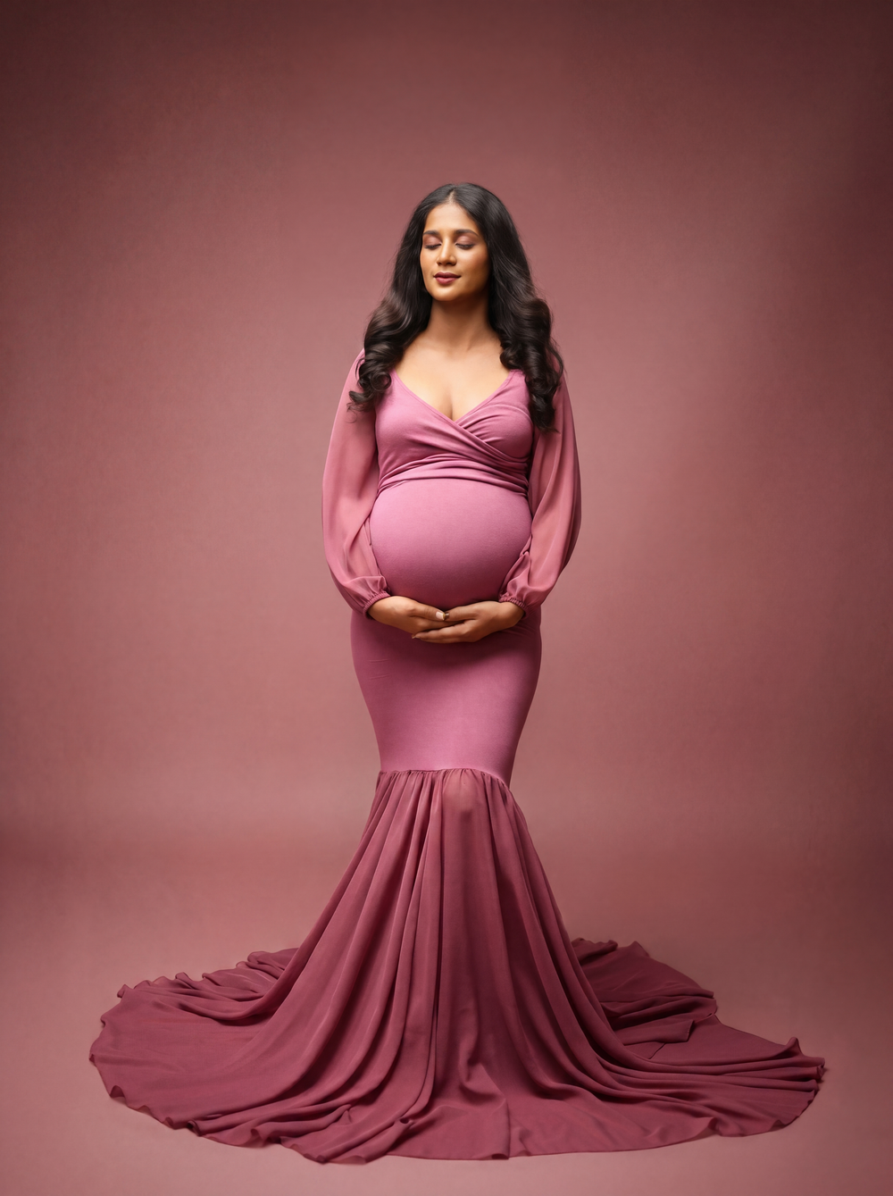 Pregnant woman in elegant mauve mermaid gown cradling baby bump during professional maternity photo session.