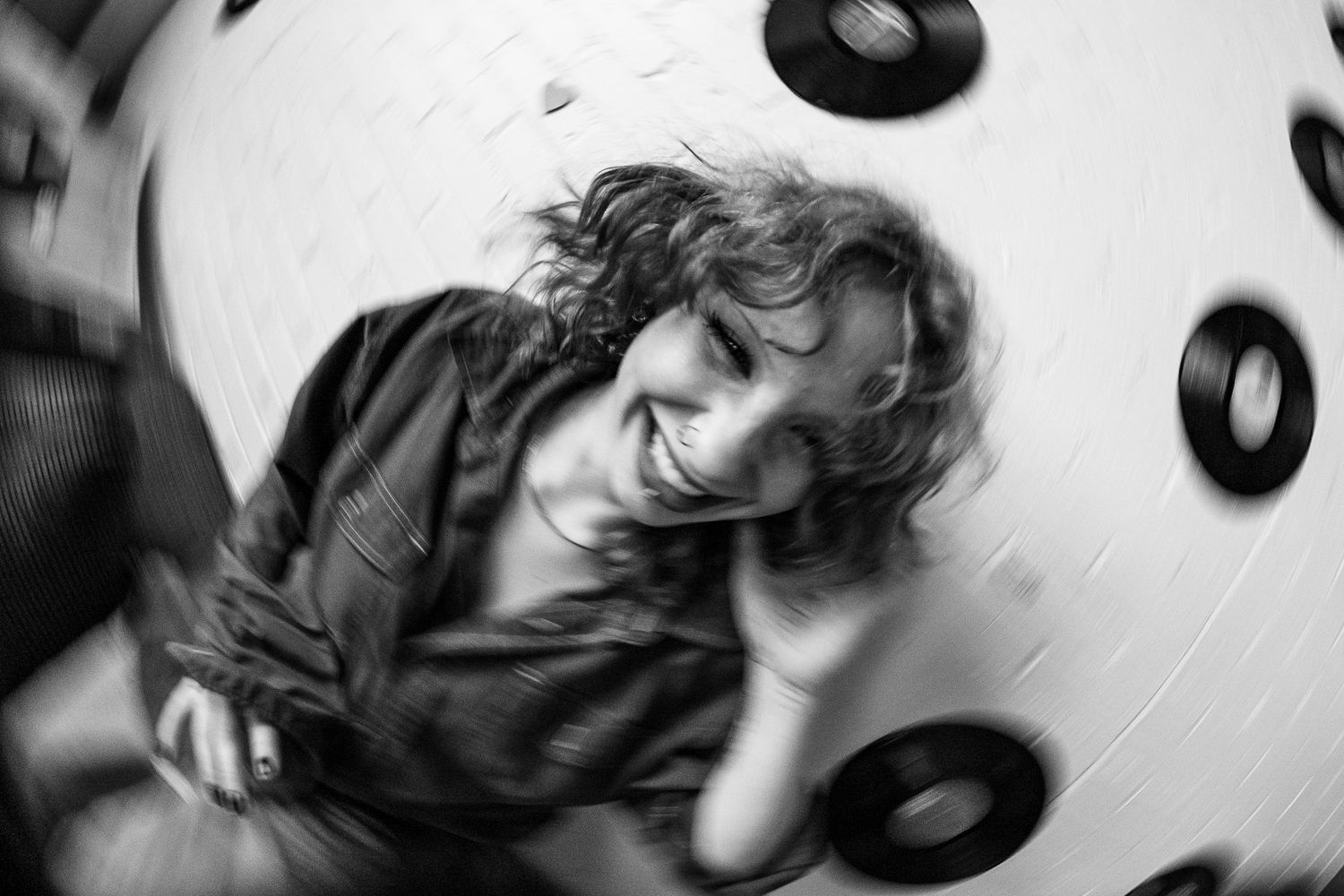 Black and white photo of a woman leaning on metal railings in an urban stairwell with checkered tiles.