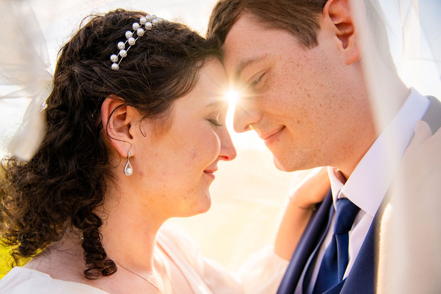 Bride and groom share a romantic close moment with sunlight glowing between them on their wedding day.