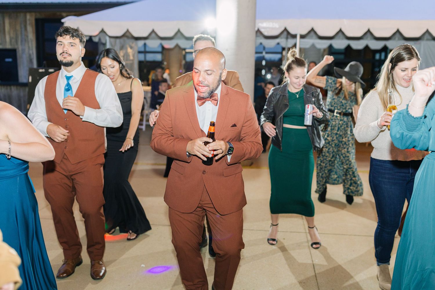 Guests in formal attire dance at a wedding reception on an elegant venue dance floor.