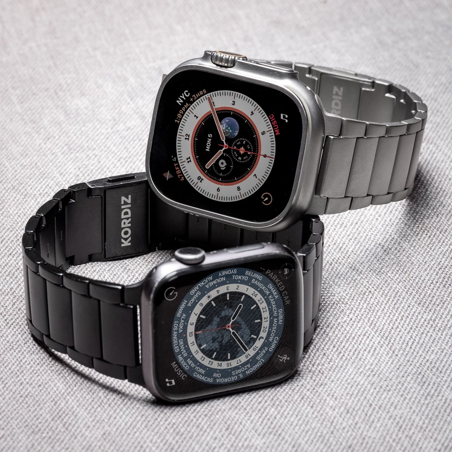 Apple Watch Ultra with metal band beside MacBook, headphones, and accessories on dark wooden surface.