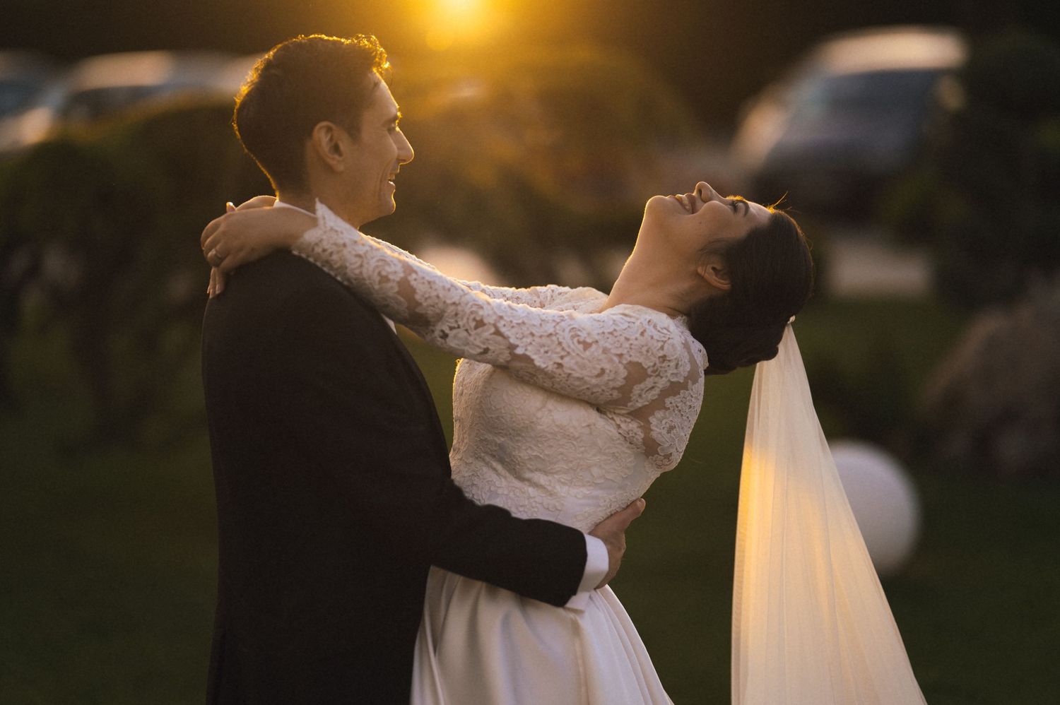 A bride and groom share a romantic embrace at sunset, with golden light glowing behind them on their wedding day.