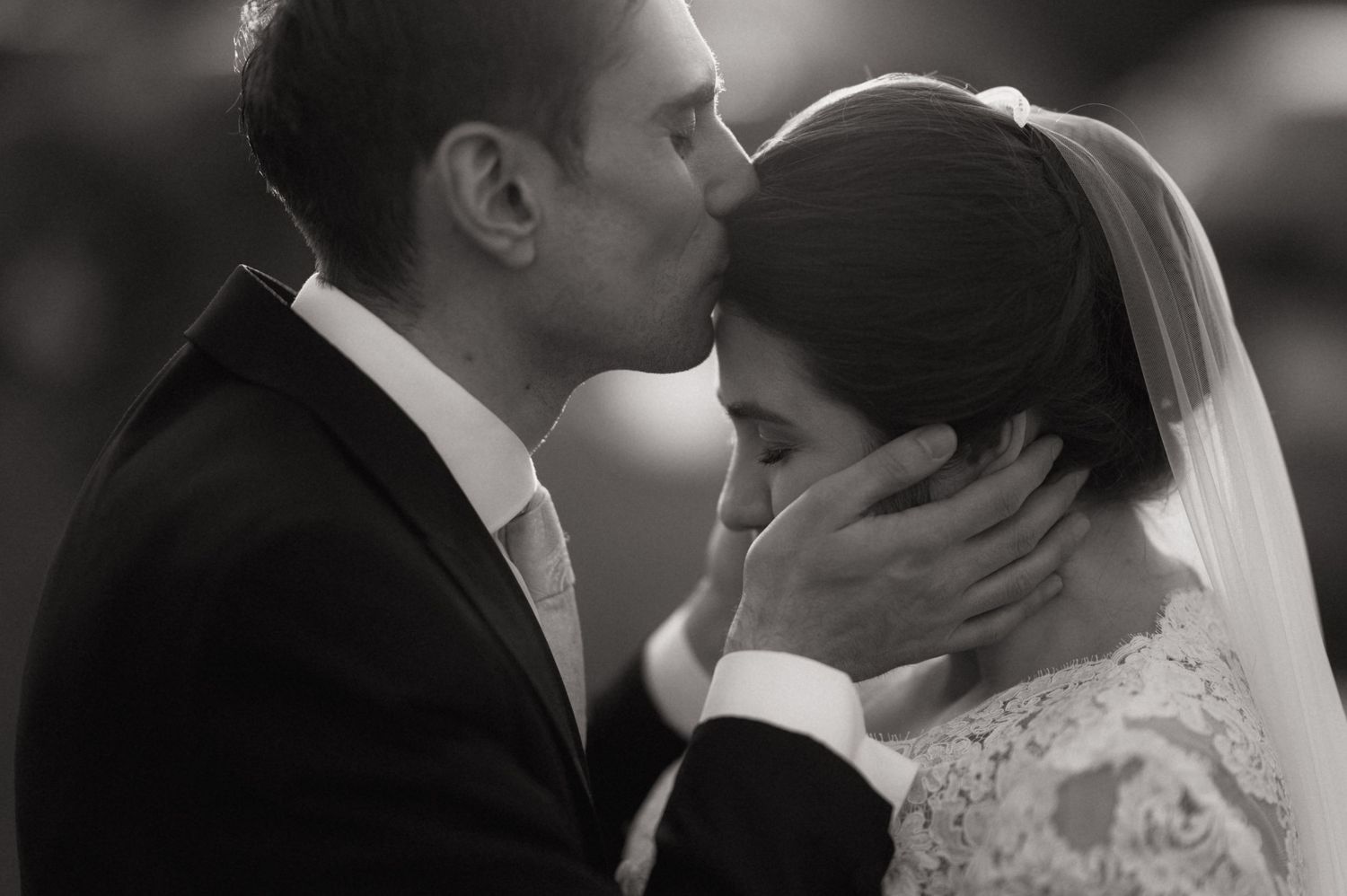 Black and white wedding photo of groom kissing bride on forehead while tenderly holding her face.