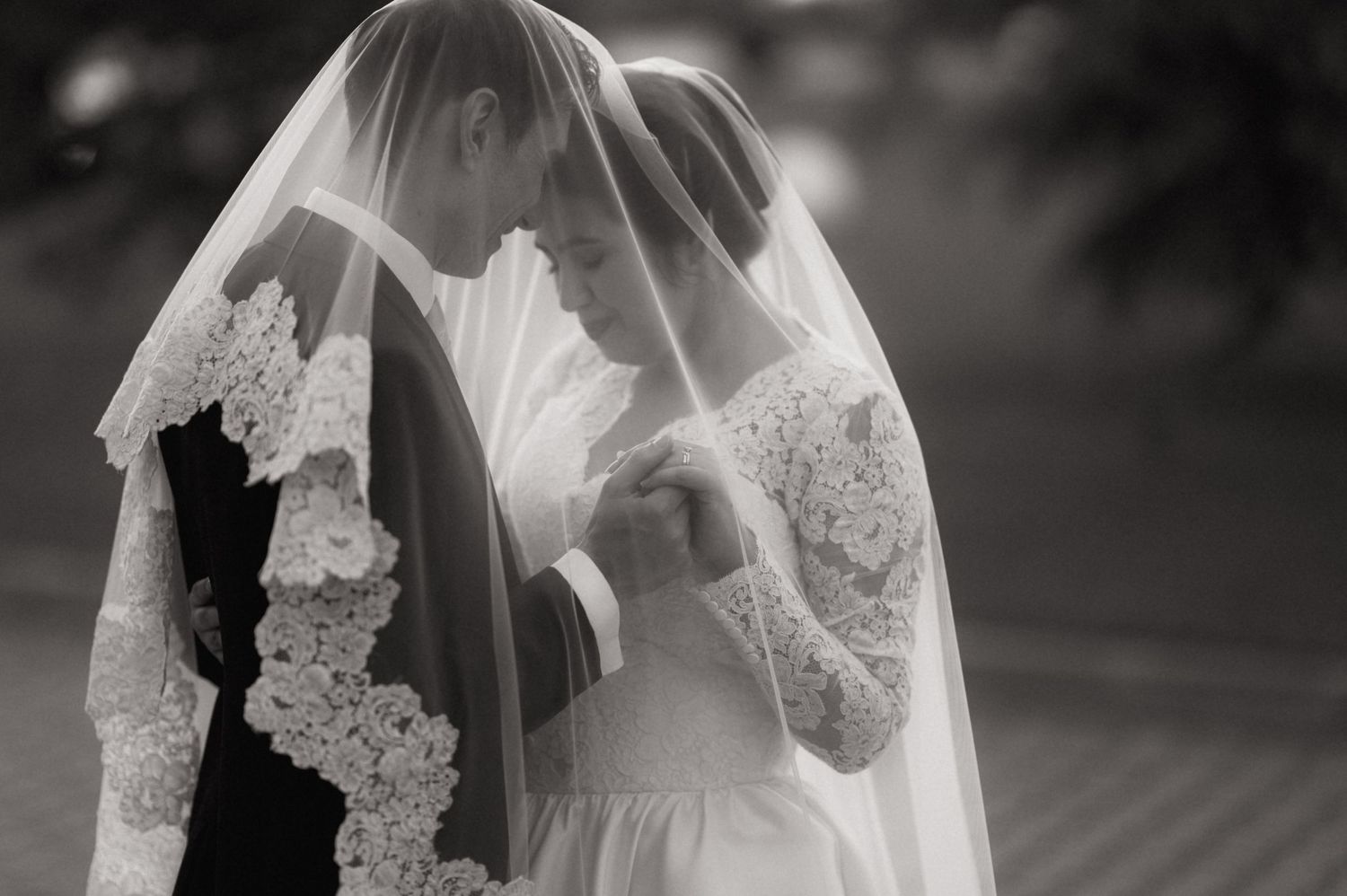 Black and white wedding photo of bride and groom sharing intimate moment under lace veil.