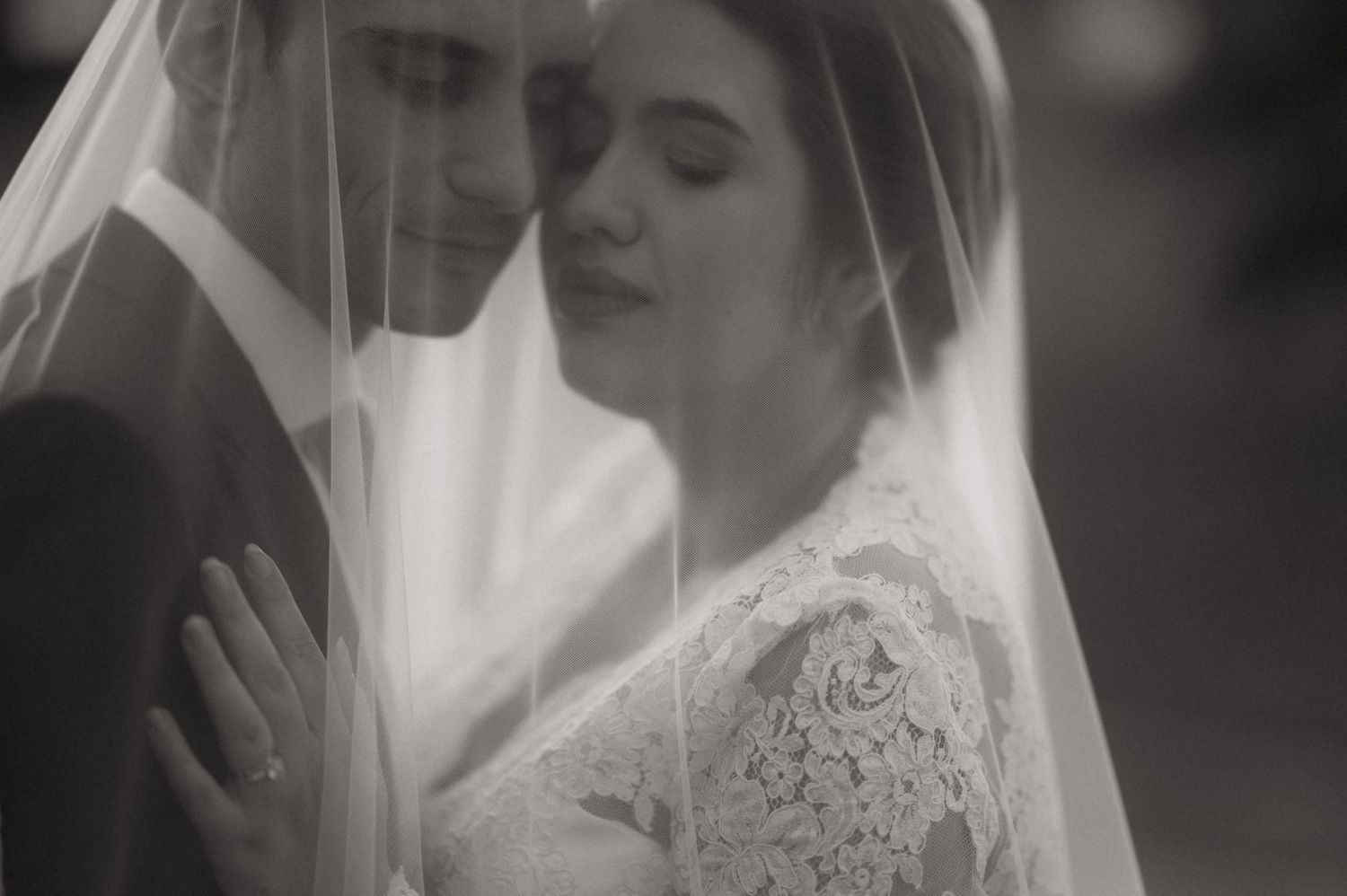 Black and white wedding photo of bride and groom sharing intimate moment under veil.