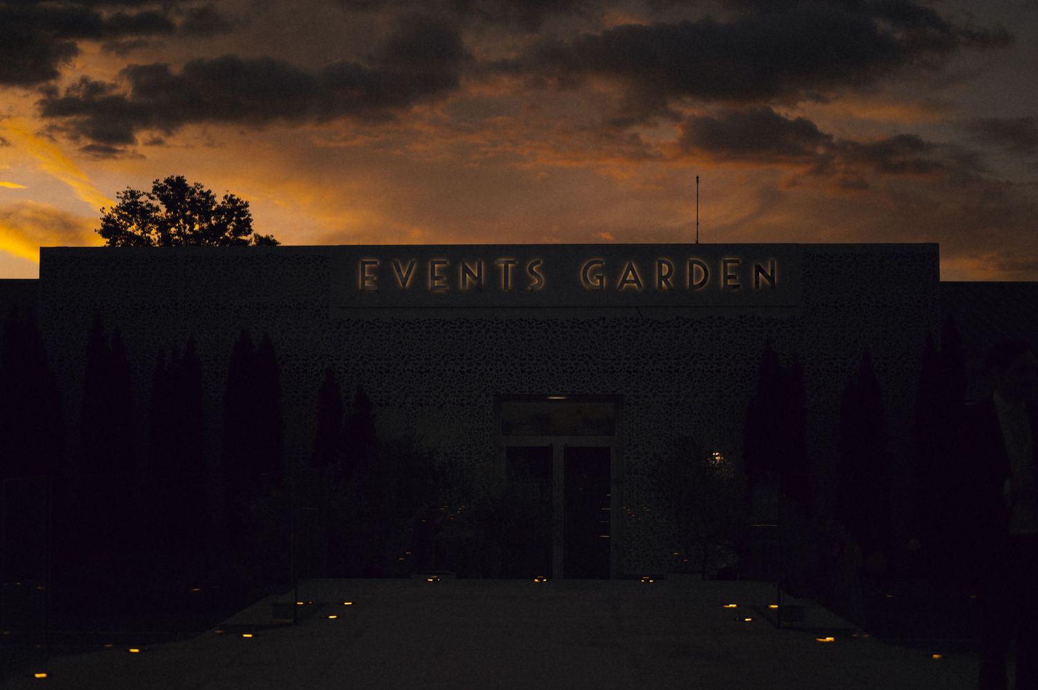 Events Garden venue illuminated at dusk with glowing signage against a dramatic orange and purple sunset sky.
