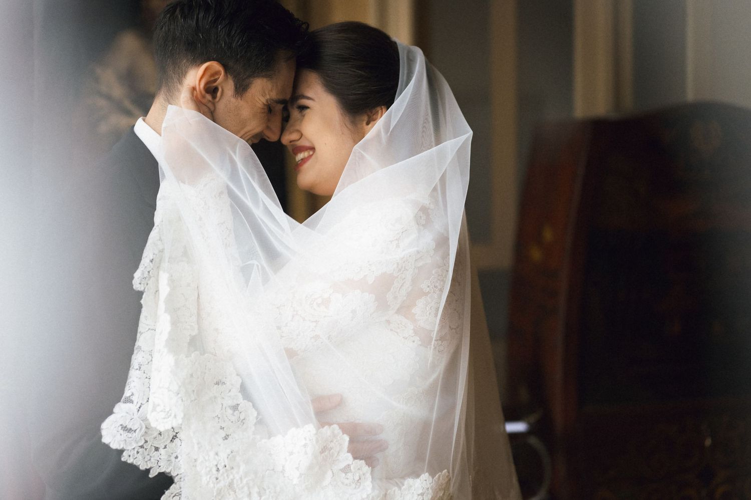 A bride and groom share an intimate moment under a white lace veil on their wedding day.