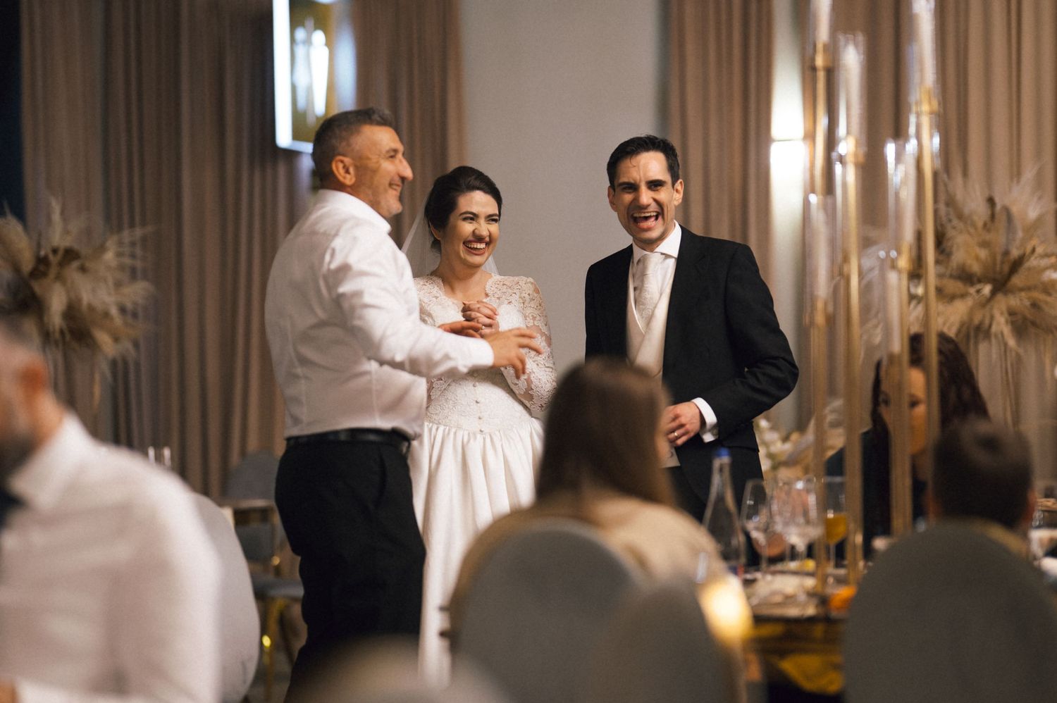Bride and groom laughing with a guest at an elegant wedding reception venue.