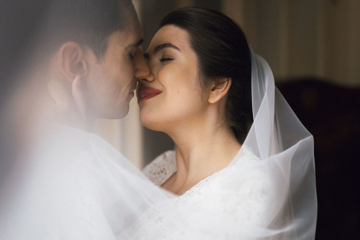 Bride and groom sharing an intimate moment, bride wearing a white veil and wedding dress with red lipstick.